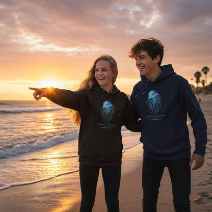 Two people wearing the bio unisex Hoodies with the Immortal Jellyfish design by seablub in Black and Blue, standing on a beach at sunset.