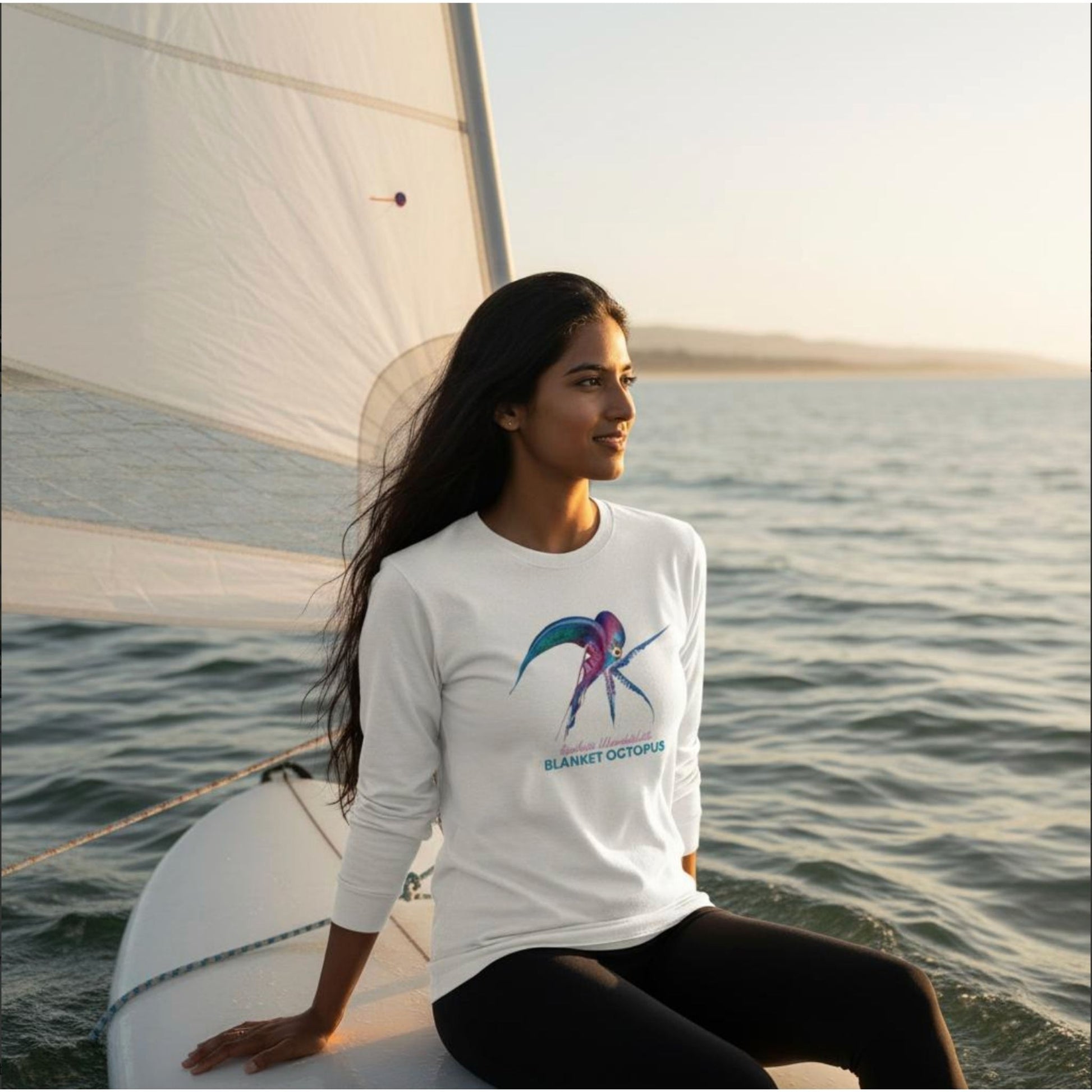 Model wearing a seablub unisex organic Long Sleeve Shirt with Blanket Octopus design in White sitting on a surfboard at sea
